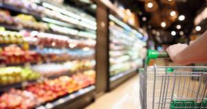 Customer pushing a shopping cart through a grocery store refrigeration section