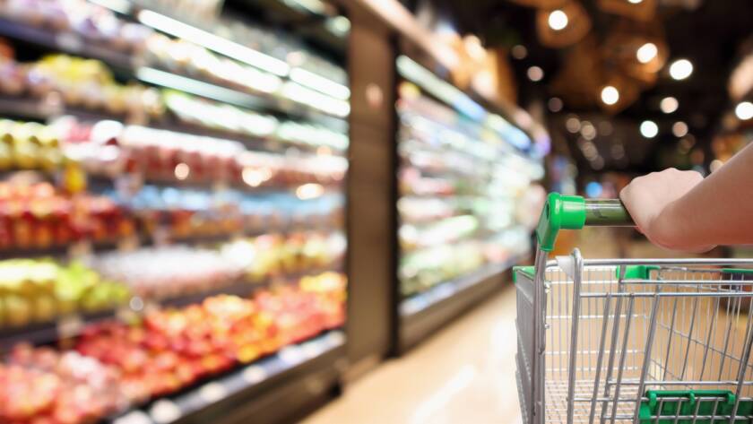 Customer pushing a shopping cart through a grocery store refrigeration section