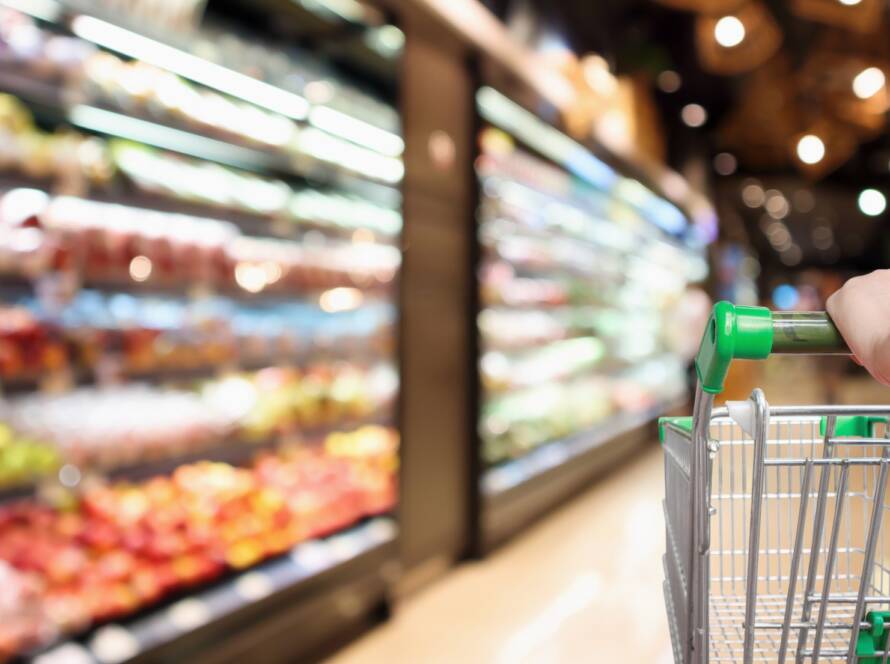 Customer pushing a shopping cart through a grocery store refrigeration section